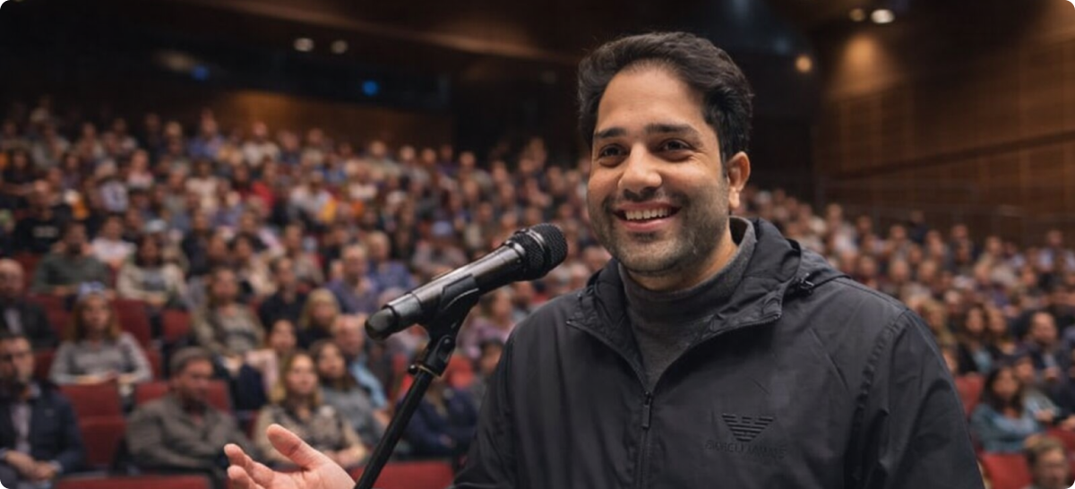 Junaid Masoodi on stage, smiling with audience in backdrop.